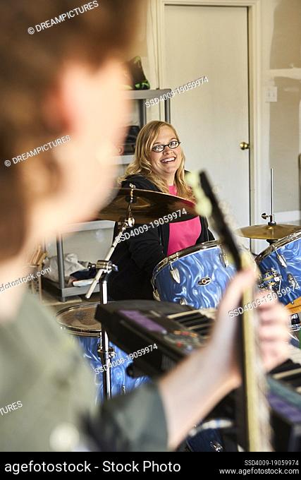 View of Drummer over guitar players shoulder in garage band composed of middle aged women, practicing in residential garage