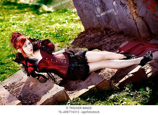 Young female wearing red corset sitting on steps outdoors