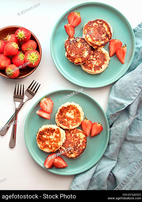Sweet cheese pancakes on plate served strawberries. Cottage cheese pancakes, syrniki, ricotta fritters, curd fritters. Top view or flat lay. Vertical