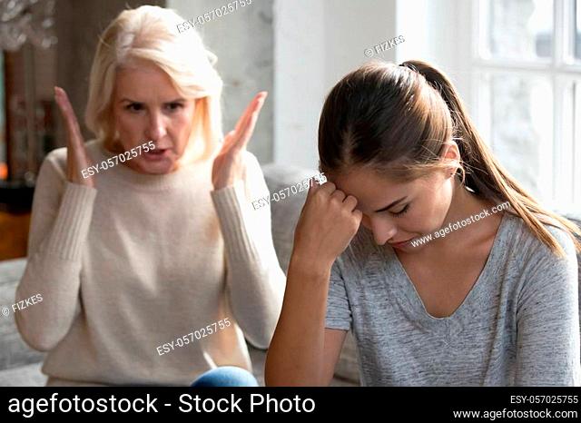 Mid aged mother sit on couch scold grown up daughter, angry mum tell complaints lecturing teen adult child feeling stressed, misunderstandings, generational gap