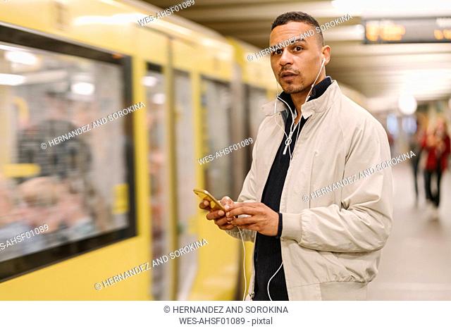 Portrait of man at underground station platform using earphones and cell phone, Berlin, Germany