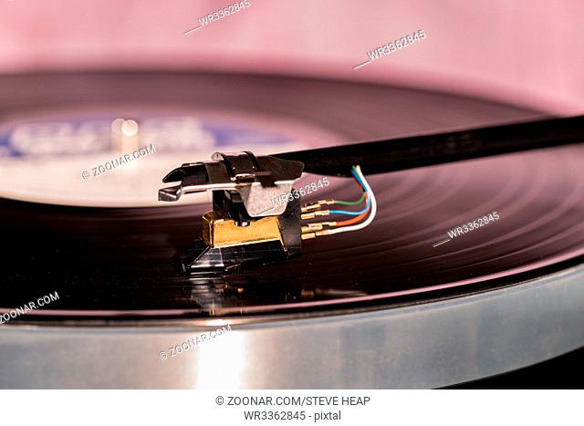 Side view of a playing vinyl record on vintage hi-fi stereo turntable with tonearm and cartridge in tracks of the LP