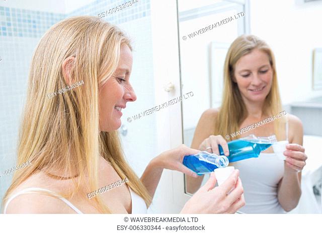 Happy woman pouring blue mouthwash at home in the bathroom