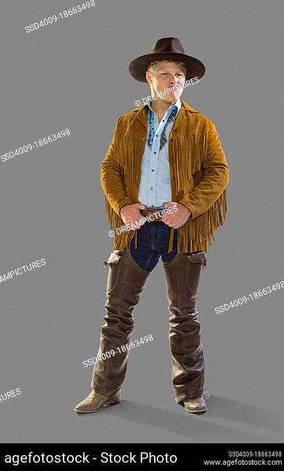Man in a cowboy costume for Halloween smiling and making at face looking off camera, against a gray background