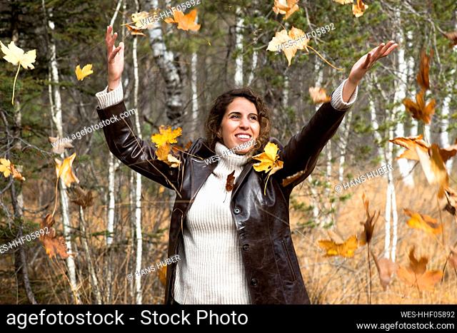 Happy woman playing with autumn leaves at forest