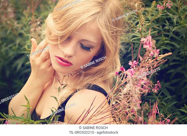 young woman with blonde hair closing her eyes and turning to the side around her pink/purple blossoms