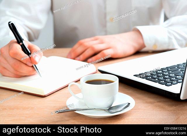 Close-up of male hand writing the to do list in notebook. Businessman at workplace with cup of coffee. Business planning and organisation