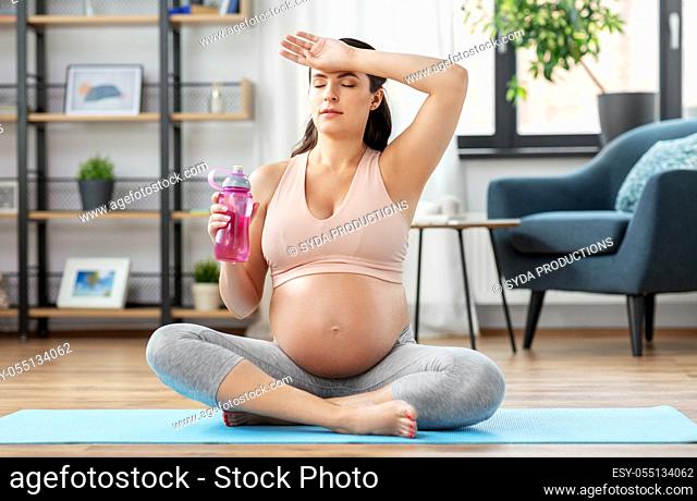 pregnant woman drinking water after yoga at home