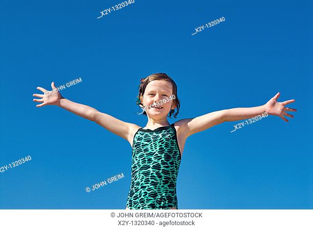 Joyous girl in bathing suit and open arms at the beach