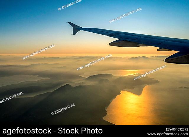 View on passenger aircraft left wing. Sun shines as a light beam over the wing. Thick clouds below airplane are illuminated by the. Golden sun