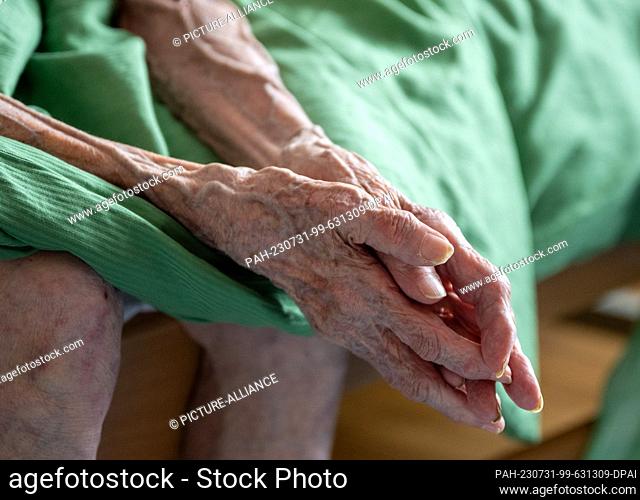 PRODUCTION - 31 July 2023, Berlin: A senior citizen in need of care sits on her bed, photographed during a visit by an outpatient nurse to the patient's home