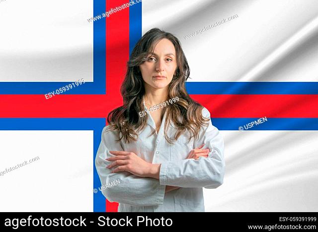 Medicine in Faroe Islands. Happy beautiful female doctor in medical coat standing with crossed arms against the background of the flag of Faroe Islands