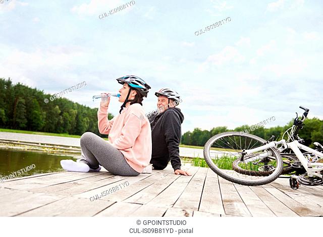 Mature couple relaxing on jetty, bicycles beside them