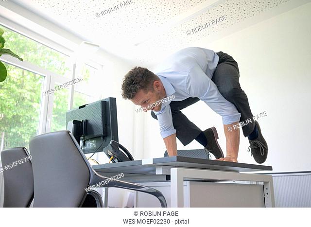Businessman balancing on desk in office