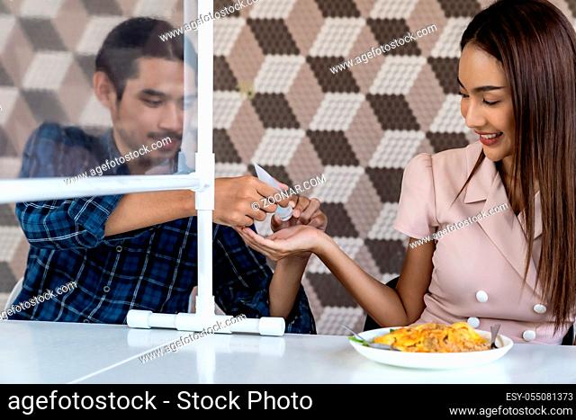 Asian man put alcohol gel to his partner befor eating at new normal social distance restaurant with table partition reduce infection of coronavirus covid-19...