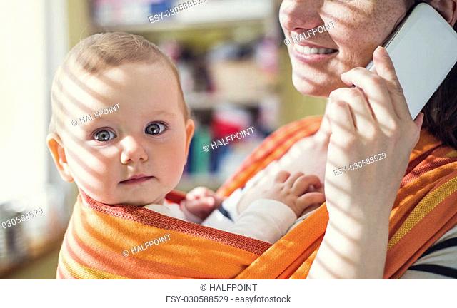 Young mother talking on a phone having her baby in a carrier