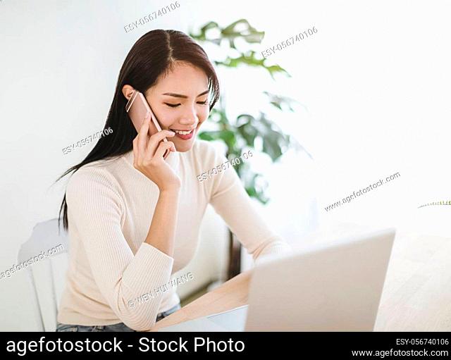 young woman working on laptop and talking on the phone at home