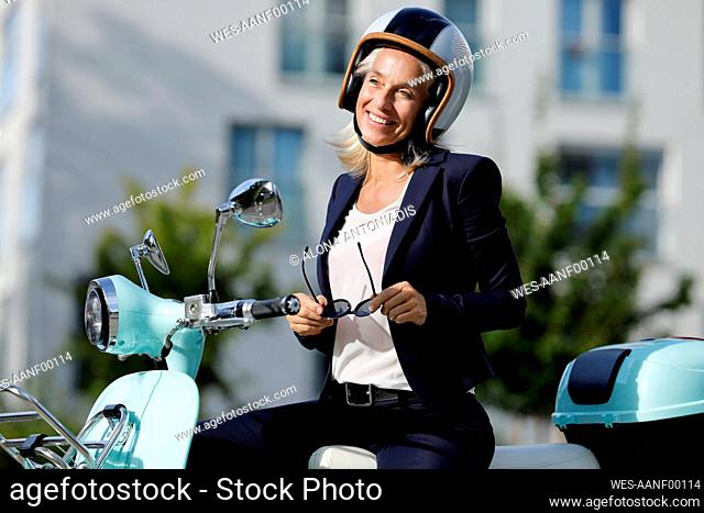 Smiling businesswoman looking away while sitting on scooter