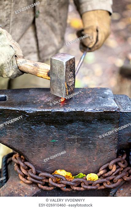 Blacksmith forges hot iron rod with sledgehammer on anvil in outdoor rural smithy