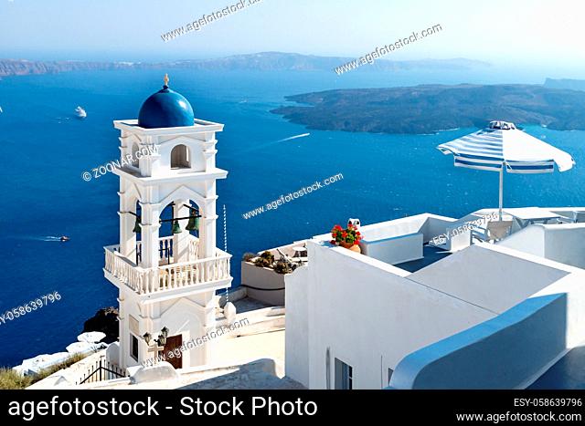 The tower of Anastasi church and parasol with ocean and islands in the background on a sunny cloudless day, Imerovigli, Santorini, Greece