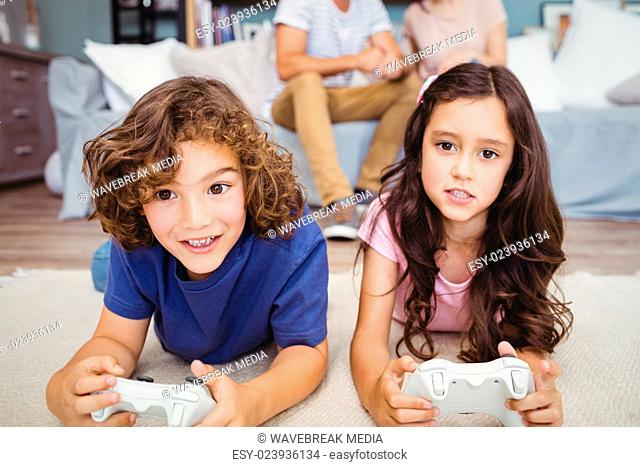 Siblings with remote playing video games on carpet