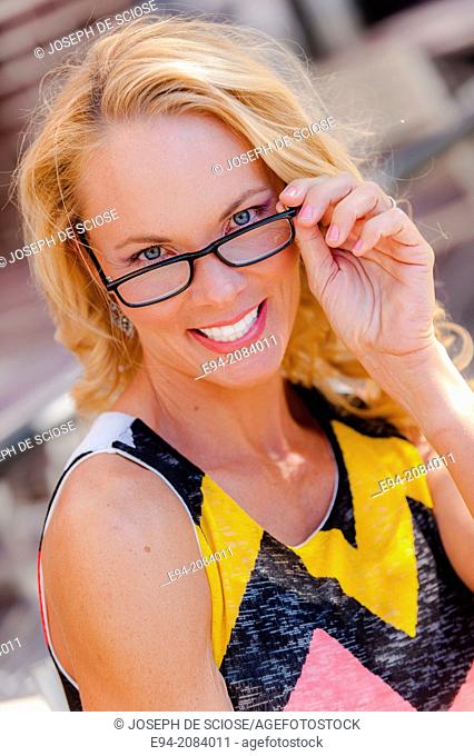 A 39 year old blond woman looking over her reading glasses smiling at the camera