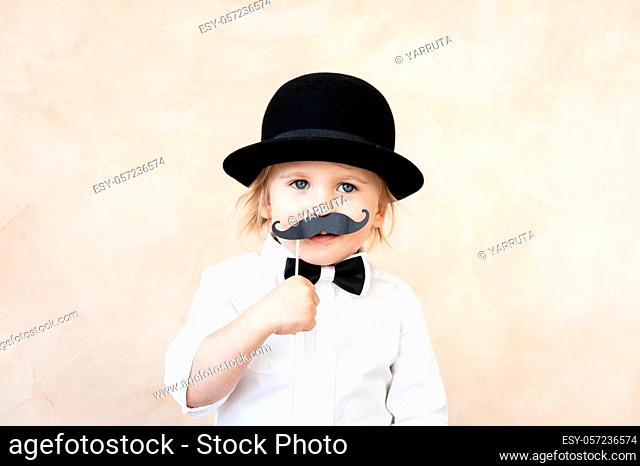 Funny kid with fake paper moustache. Happy child playing in home. Father's day concept