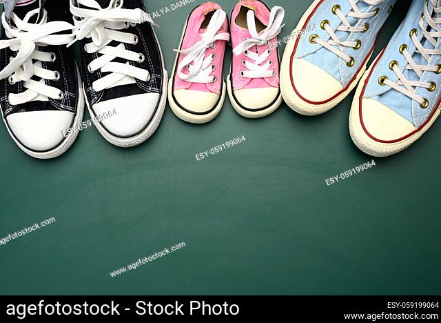 many multi-colored well-worn textile sneakers of different sizes on a green background, top view, concept family, copy space