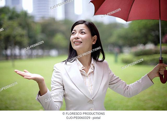 Businesswoman outdoors in park holding umbrella