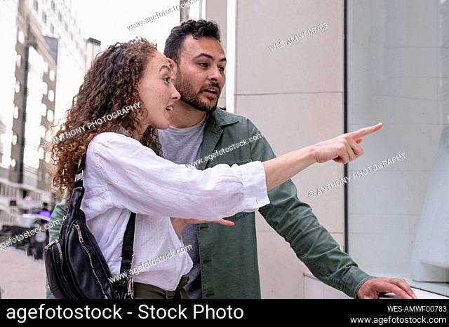 Excited woman pointing at store window standing by man