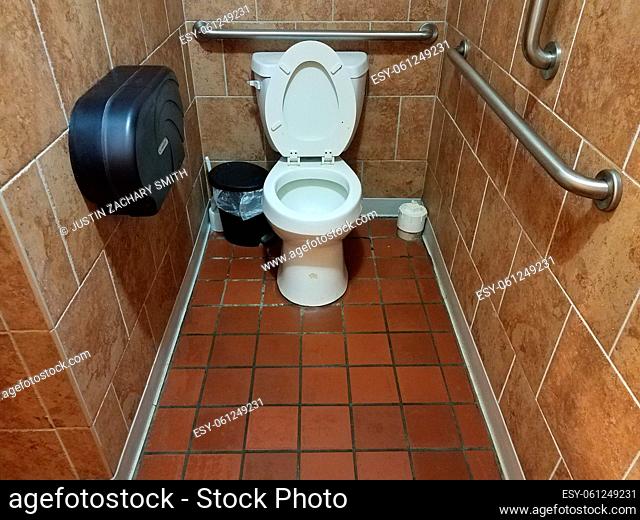bathroom stall with toilet and tiled floors and rails
