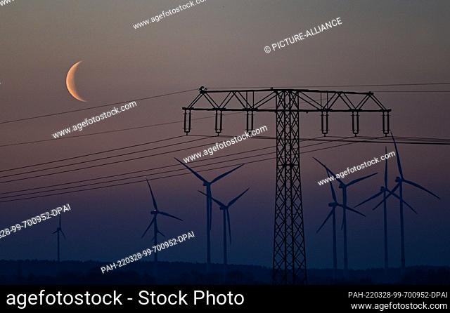 28 March 2022, Brandenburg, Sieversdorf: The waning moon is seen at dawn over the landscape with a power line and wind turbines in East Brandenburg