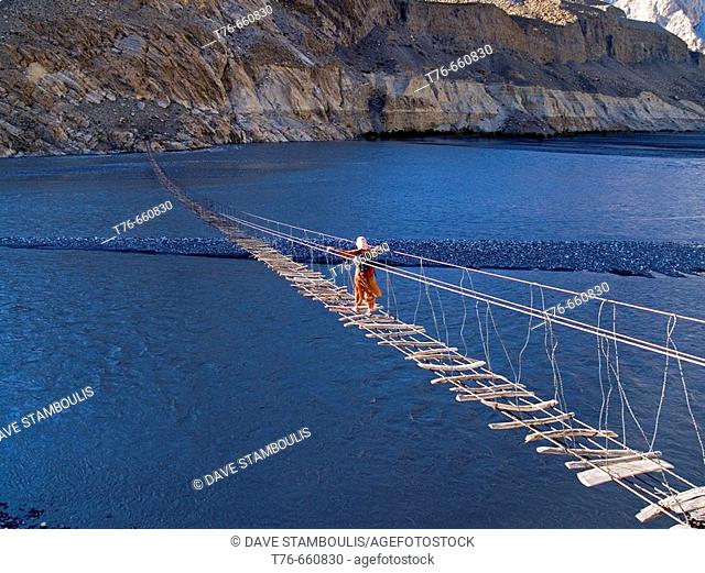 Trekker makes the scary crossing of the Hunza River in the Karakoram Mountains of Pakistan on rickety footbridge