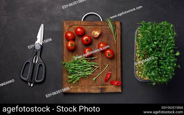 Red tomato and sprouted pea seeds on a black background, microgreens for salad, detox. Top view