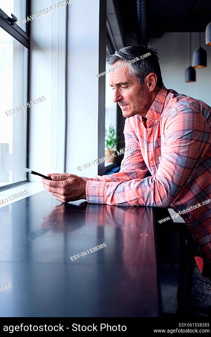 Caucasian mature businessman text messaging through mobile phone in creative office
