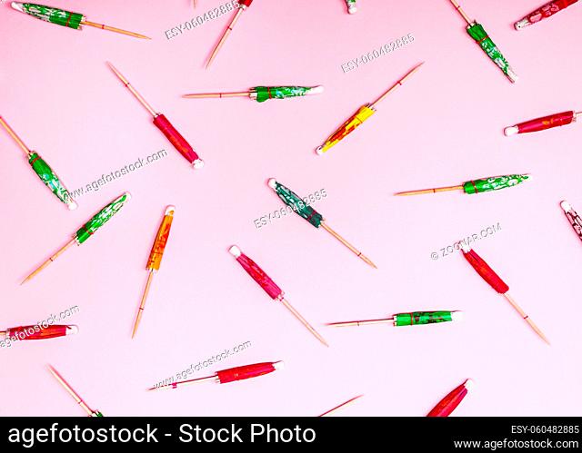 colorful wooden cocktail umbrellas folded on a pink background, top view