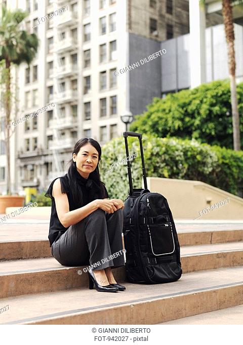 A businesswoman sitting on a step next to a rolling suitcase