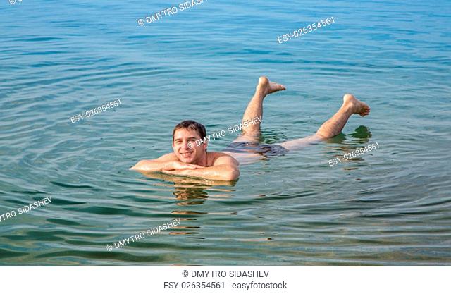 Man floating in the Dead Sea in Jordan. Dense salty water pushes the man out. Smiling man swims in the sea
