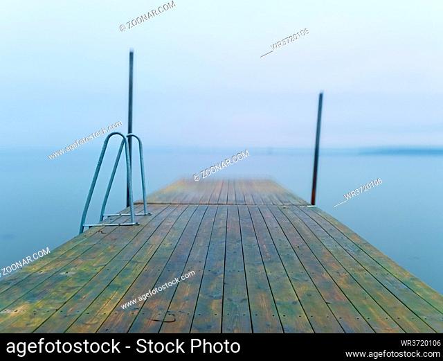 Abandoned wooden wharf mole in sea within sunrise. Gentle blue pink color of sky blurry waves on water level