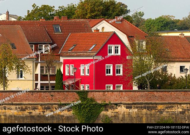06 October 2023, Saxony, Torgau: 06.10.2023, Torgau. A pretty, red house stands in Torgau next to other residential buildings above the banks of the Elbe