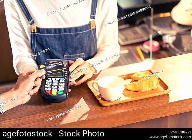 Close-up of asian customer using his credit card with contactless nfs technology to pay a barista for his coffee purchase at a cafe bar