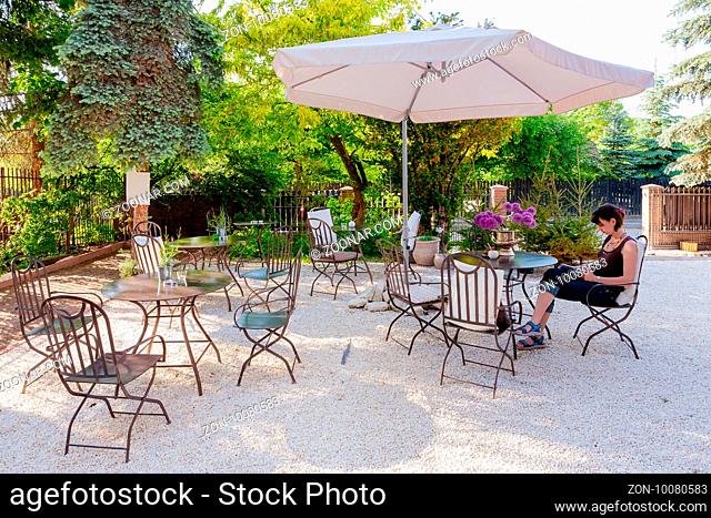 Tables and chairs of outdoor cafe with single female tourist