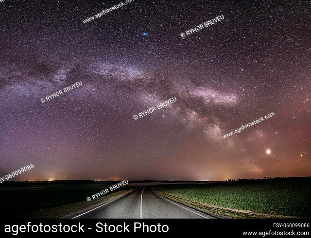 Magenta Night Starry Sky Above Country Asphalt Road In Countryside And Green Field. Night View Of Natural Glowing Stars And Milky Way Galaxy