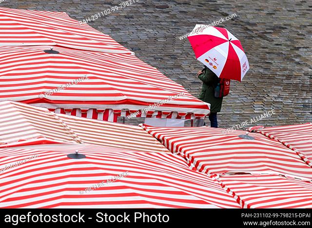 02 November 2023, Bavaria, Nuremberg: A woman walks in rainy weather with an umbrella across the main market past the red and white striped roofs of the market...