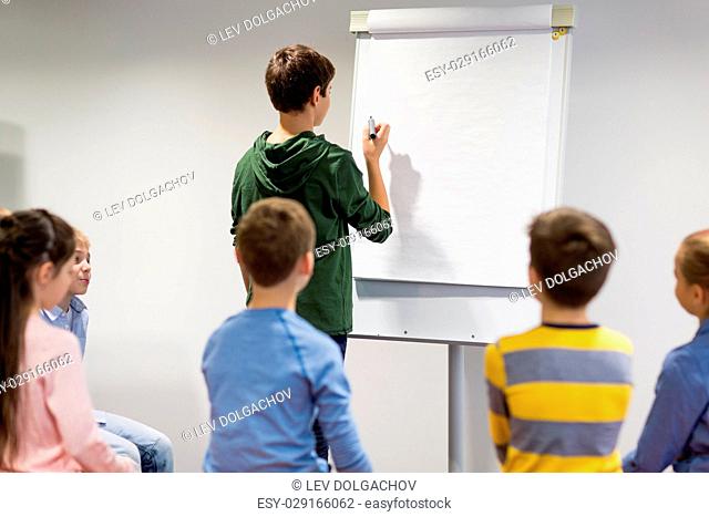 education, elementary school, learning and people concept - student boy with marker writing on flip board