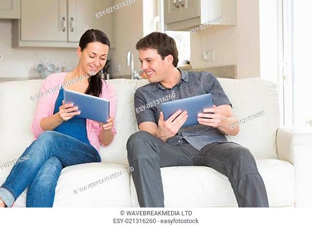 Two people sitting on the couch in the living room while using a tablet computer