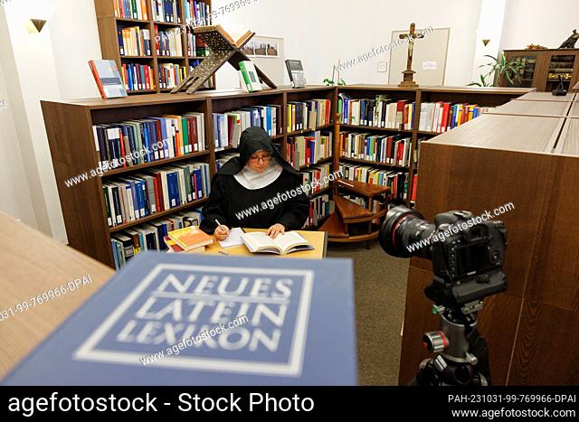 PRODUCTION - 20 October 2023, Lower Saxony, Osnabrück: Sister Josefine sits in a posed situation in a room of the Osnabrück Diocesan Library behind a book...
