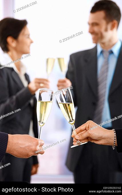 Business people raising toast with champagne at office, focus placed on flutes
