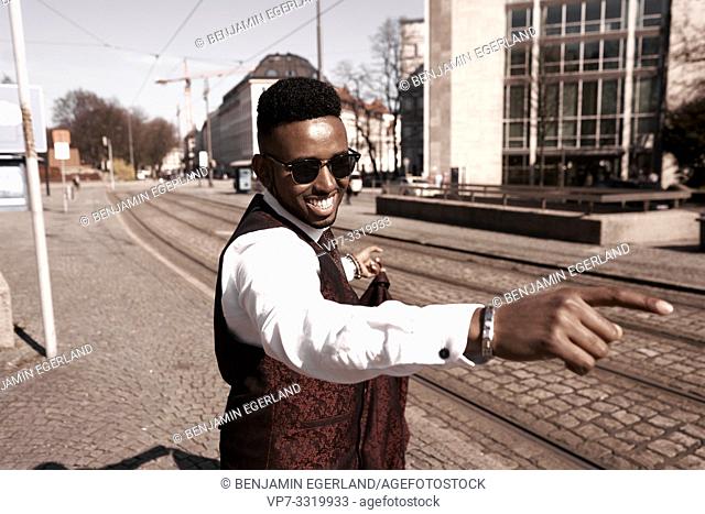 motivated well-dressed African man pointing forward, wearing fancy red suit at street in city, in Munich, Germany