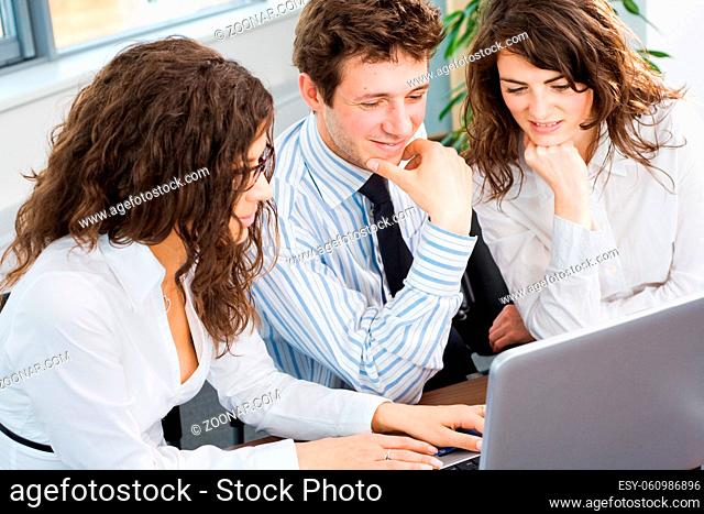 Happy team of young business people sitting in meeting room, working together on laptop computer, smiling. Overhead view